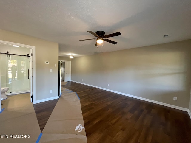 empty room with a barn door, ceiling fan, a textured ceiling, and dark hardwood / wood-style flooring