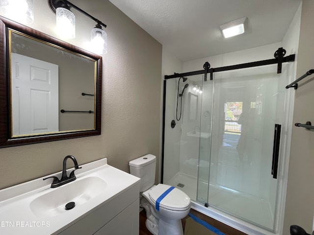 bathroom with vanity, toilet, a textured ceiling, and a shower with door