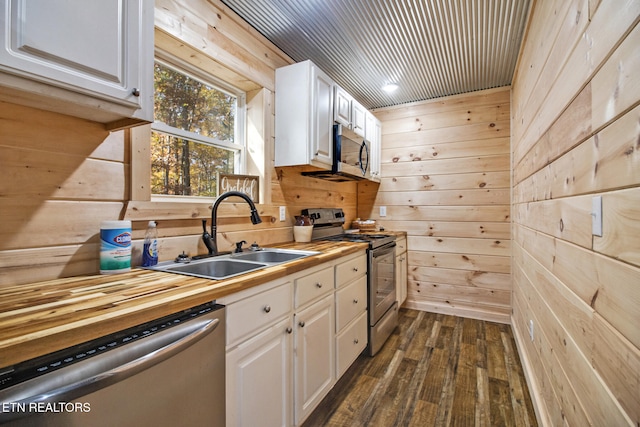 kitchen featuring white cabinetry, stainless steel appliances, and wood walls