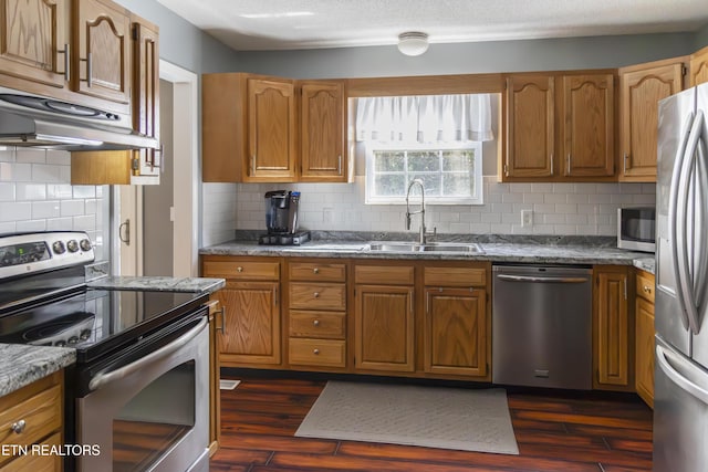 kitchen with decorative backsplash, appliances with stainless steel finishes, sink, stone countertops, and range hood