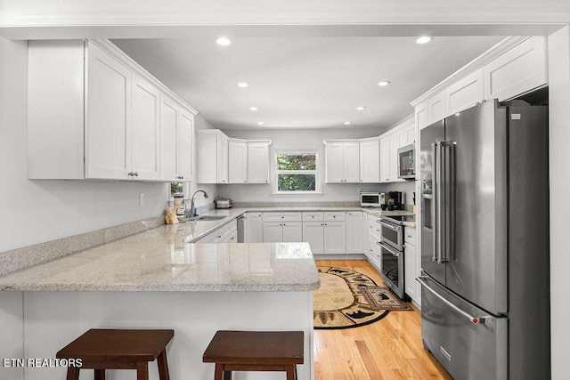 kitchen with sink, stainless steel appliances, kitchen peninsula, a kitchen bar, and white cabinets