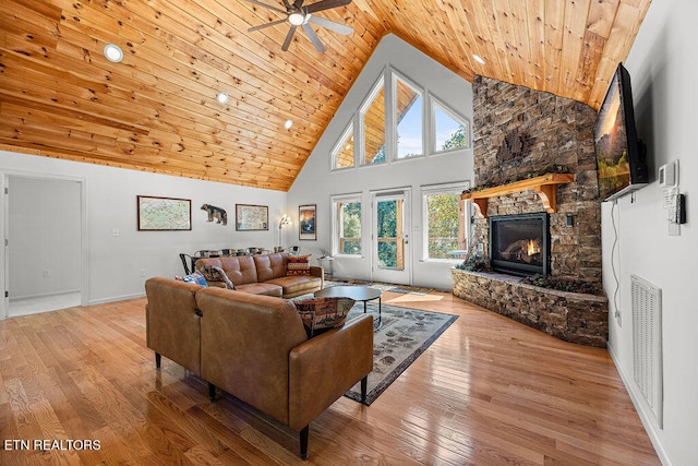 living room featuring light hardwood / wood-style floors, a stone fireplace, wood ceiling, and high vaulted ceiling