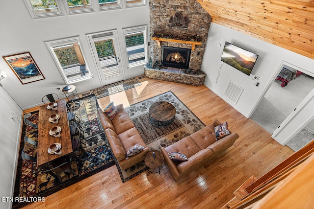 living room with hardwood / wood-style flooring, a stone fireplace, and a high ceiling