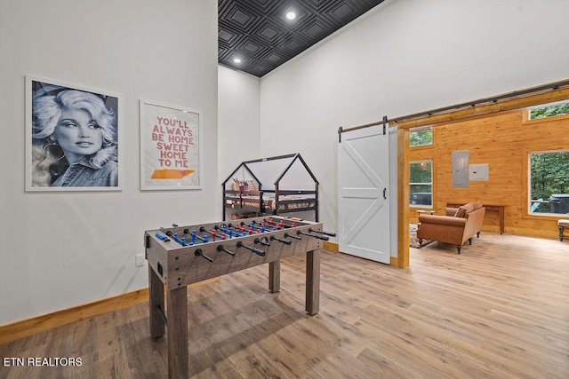 game room with a barn door, wooden walls, light hardwood / wood-style floors, and a high ceiling