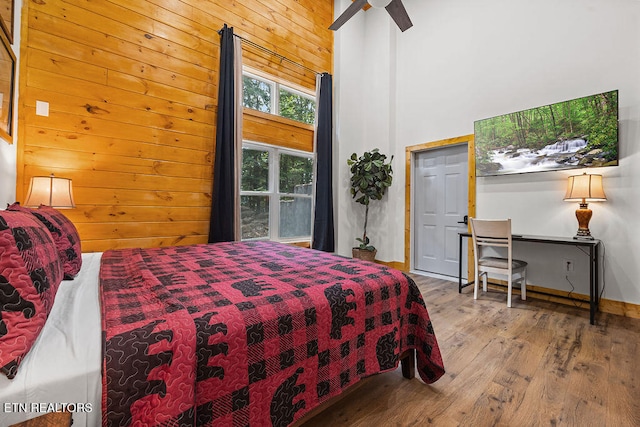 bedroom featuring ceiling fan, light hardwood / wood-style flooring, a high ceiling, and wooden walls