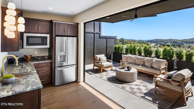 kitchen featuring built in microwave, hanging light fixtures, stainless steel refrigerator with ice dispenser, sink, and light hardwood / wood-style flooring