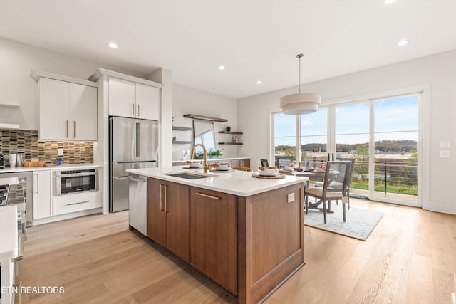 kitchen featuring a center island with sink, appliances with stainless steel finishes, decorative light fixtures, light hardwood / wood-style floors, and white cabinets