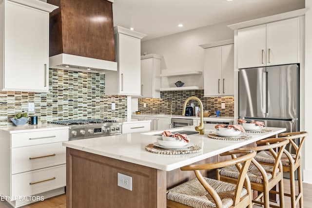 kitchen featuring stainless steel appliances, light hardwood / wood-style floors, a breakfast bar area, an island with sink, and wall chimney range hood