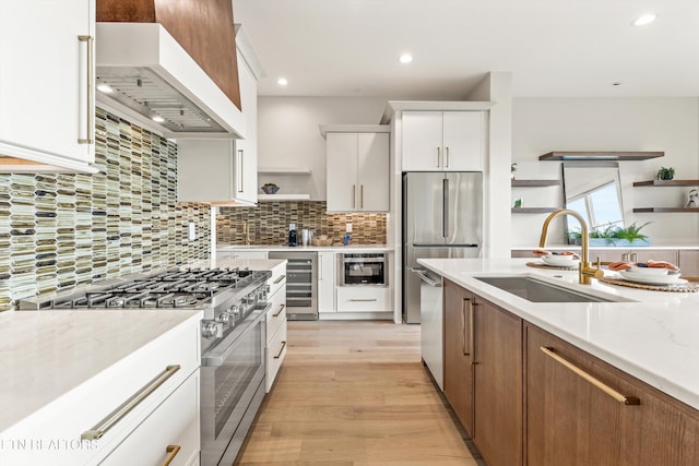 kitchen featuring white cabinetry, appliances with stainless steel finishes, custom range hood, light wood-type flooring, and light stone countertops