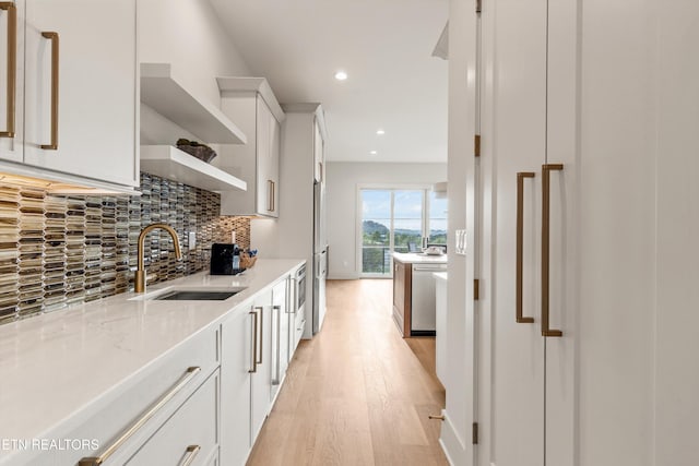 kitchen featuring white cabinets, light hardwood / wood-style flooring, sink, and light stone counters