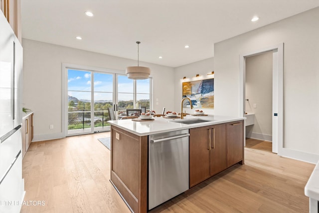 kitchen with sink, light wood-type flooring, stainless steel dishwasher, an island with sink, and pendant lighting