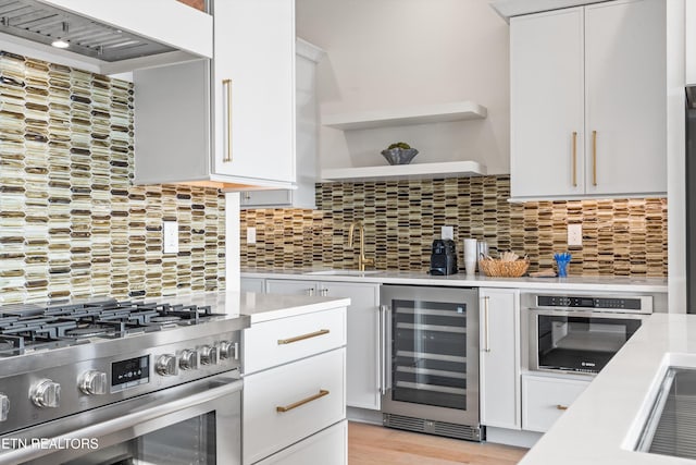 kitchen featuring light hardwood / wood-style floors, white cabinetry, appliances with stainless steel finishes, backsplash, and beverage cooler