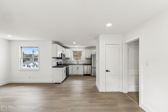 kitchen with appliances with stainless steel finishes, sink, light wood-type flooring, white cabinetry, and decorative backsplash