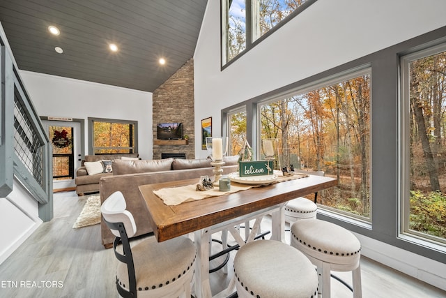 dining room featuring a wealth of natural light, a stone fireplace, light wood-type flooring, and high vaulted ceiling