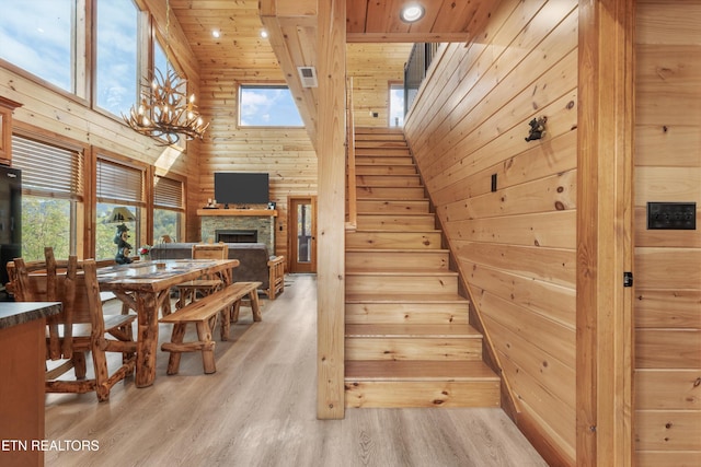 stairway with a towering ceiling, a stone fireplace, wood walls, hardwood / wood-style floors, and wooden ceiling