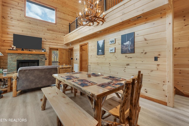 dining area featuring a fireplace, wood walls, light wood-type flooring, and a towering ceiling