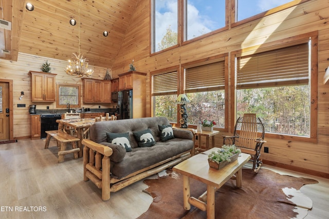 living room with high vaulted ceiling, wooden walls, a notable chandelier, and light hardwood / wood-style floors