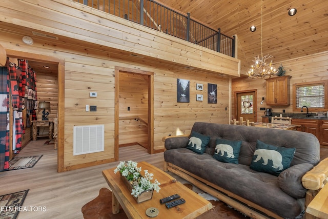 living room with a towering ceiling, wood ceiling, an inviting chandelier, wooden walls, and light hardwood / wood-style flooring