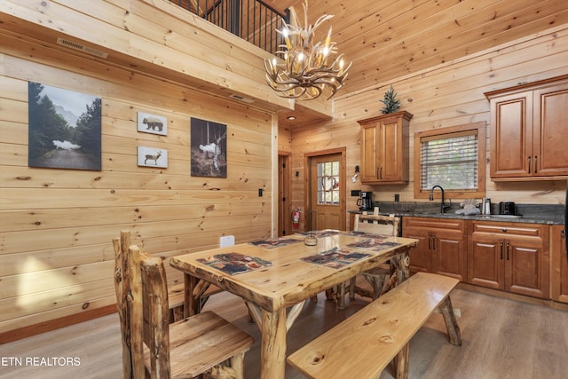 dining area with light hardwood / wood-style floors, a chandelier, wooden walls, and a high ceiling