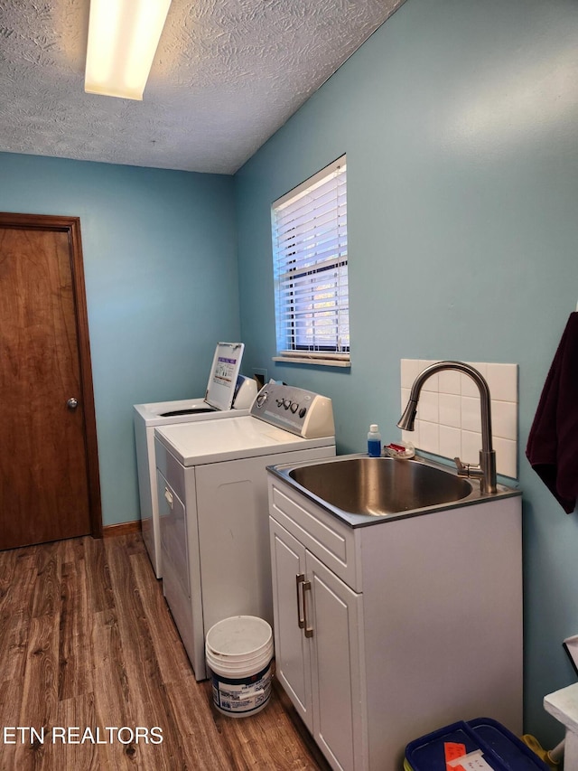 clothes washing area featuring washing machine and dryer, sink, a textured ceiling, dark wood-type flooring, and cabinets