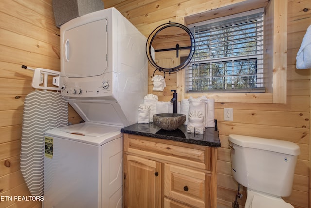 clothes washing area featuring wood walls, sink, and stacked washer / dryer