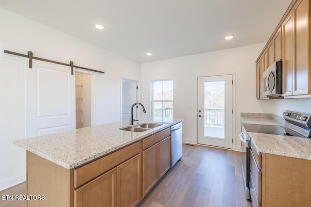 kitchen featuring stainless steel appliances, sink, wood-type flooring, a barn door, and a center island with sink