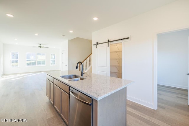 kitchen with a barn door, sink, stainless steel dishwasher, and light wood-type flooring