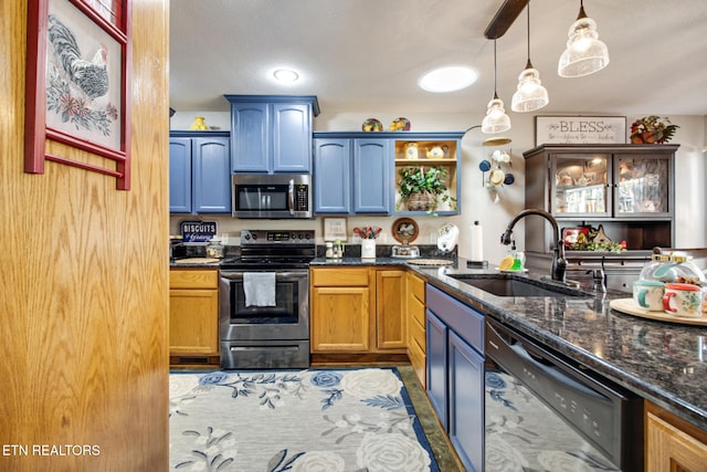 kitchen with appliances with stainless steel finishes, sink, dark stone counters, and pendant lighting