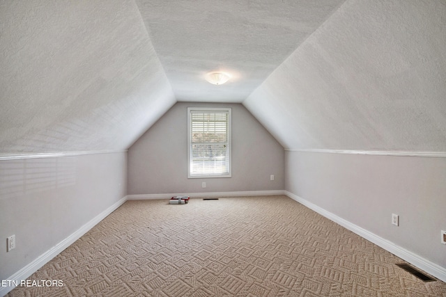 additional living space with vaulted ceiling, a textured ceiling, and carpet flooring