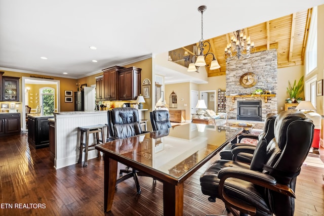 dining room with dark hardwood / wood-style flooring, vaulted ceiling, ornamental molding, a stone fireplace, and a notable chandelier