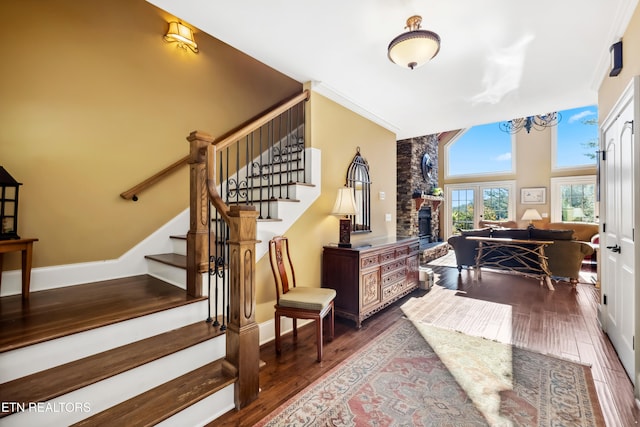 stairway featuring a towering ceiling, wood-type flooring, a fireplace, a notable chandelier, and ornamental molding