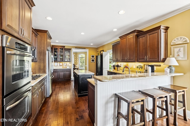 kitchen featuring kitchen peninsula, light stone countertops, ornamental molding, dark wood-type flooring, and stainless steel appliances