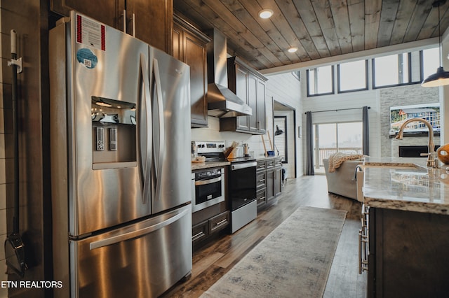 kitchen featuring wall chimney range hood, dark brown cabinets, appliances with stainless steel finishes, and wooden ceiling