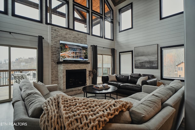 living room featuring high vaulted ceiling, a wealth of natural light, wooden walls, and a stone fireplace