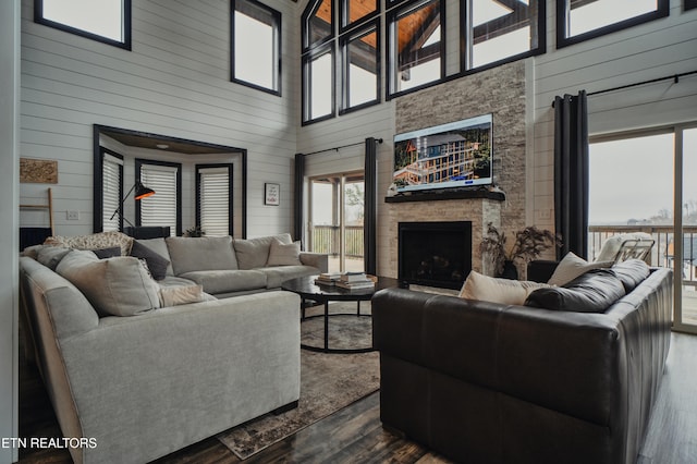 living room with a towering ceiling, a stone fireplace, wooden walls, and dark wood-type flooring