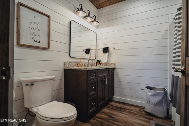 bathroom featuring toilet, a shower with curtain, wooden walls, vanity, and hardwood / wood-style flooring