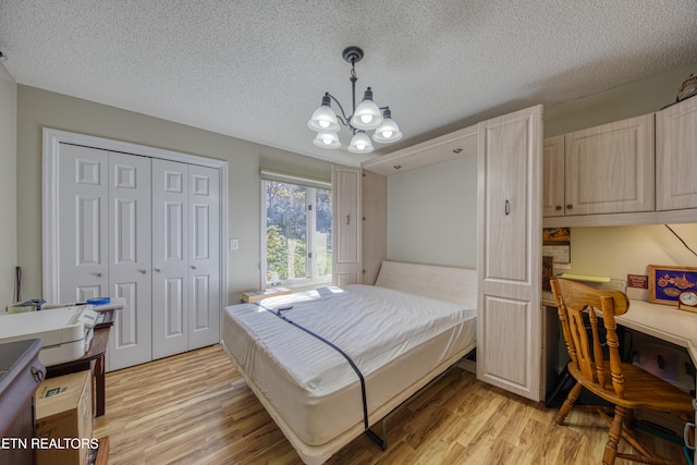 bedroom featuring a closet, light hardwood / wood-style floors, a textured ceiling, and an inviting chandelier