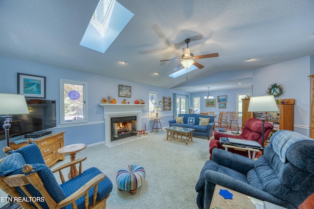 carpeted living room featuring vaulted ceiling with skylight, a textured ceiling, and ceiling fan with notable chandelier