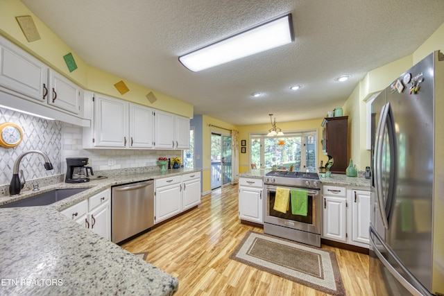 kitchen featuring sink, light hardwood / wood-style floors, stainless steel appliances, pendant lighting, and white cabinets