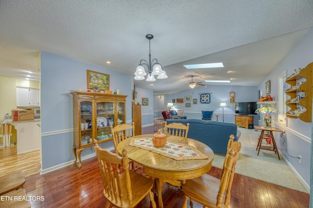 dining area with lofted ceiling with skylight, a textured ceiling, ceiling fan with notable chandelier, and light wood-type flooring