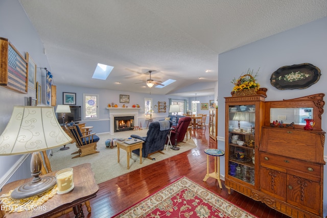 living room featuring a textured ceiling, vaulted ceiling with skylight, wood-type flooring, and ceiling fan