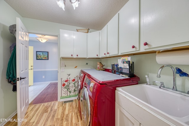 clothes washing area featuring cabinets, a textured ceiling, light wood-type flooring, sink, and washer and clothes dryer