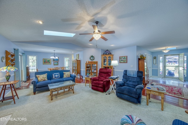 living room with lofted ceiling with skylight, carpet floors, ceiling fan with notable chandelier, and plenty of natural light