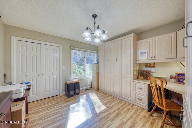 office space with built in desk, light hardwood / wood-style flooring, a notable chandelier, and a textured ceiling