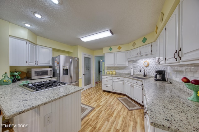 kitchen with decorative backsplash, white cabinets, light wood-type flooring, sink, and stainless steel appliances