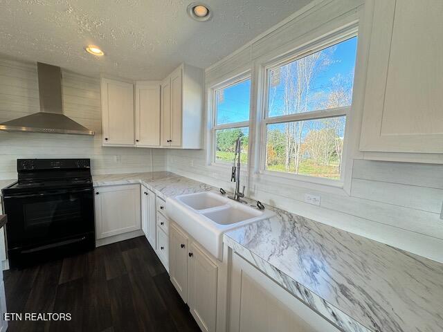 kitchen featuring wall chimney range hood, black range with electric cooktop, sink, white cabinetry, and a textured ceiling