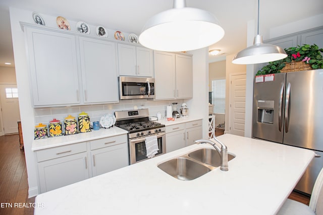 kitchen with a wealth of natural light, sink, hanging light fixtures, stainless steel appliances, and hardwood / wood-style flooring