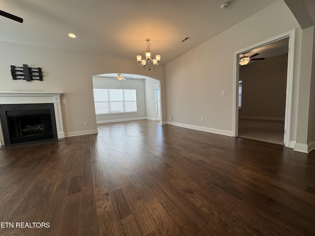 unfurnished living room with ceiling fan with notable chandelier and dark wood-type flooring