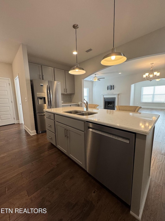 kitchen featuring appliances with stainless steel finishes, dark wood-type flooring, sink, a center island with sink, and gray cabinets