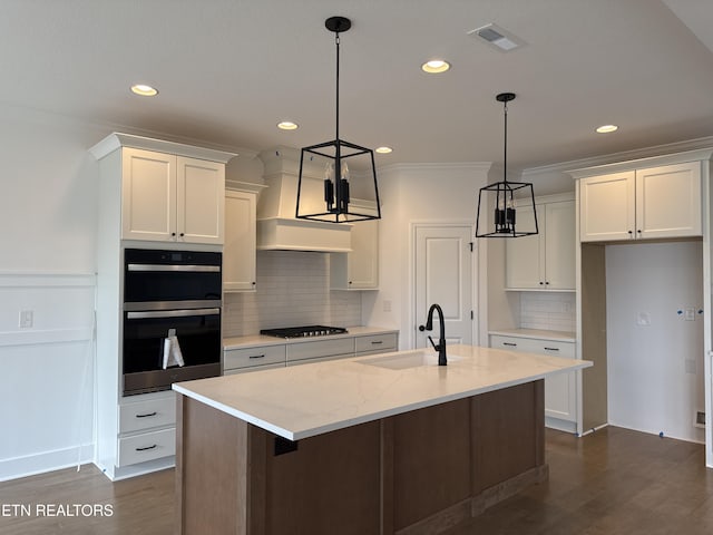 kitchen with stainless steel gas cooktop, white cabinetry, double oven, pendant lighting, and a kitchen island with sink